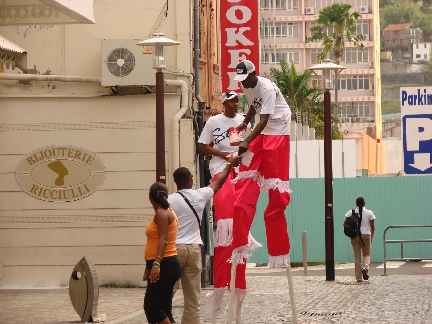 Échassiers en costume distribuant des flyers aux passants dans une rue commerçante des Antilles
